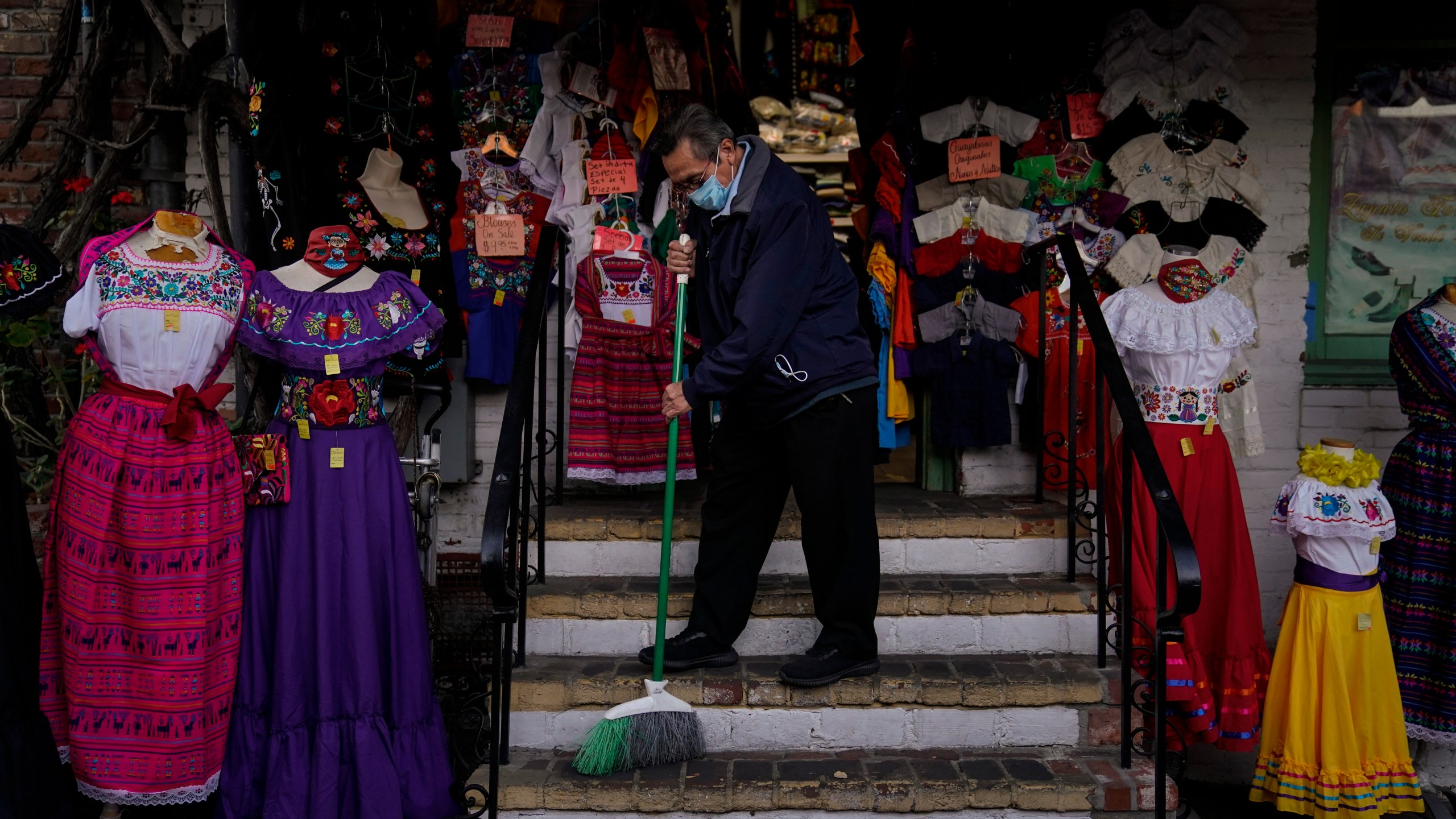 Victor Flores, 66, a third-generation owner of a gift shop, sweeps the steps of his store on Olvera Street in downtown Los Angeles on Dec. 16, 2020. (Jae C. Hong / Associated Press)