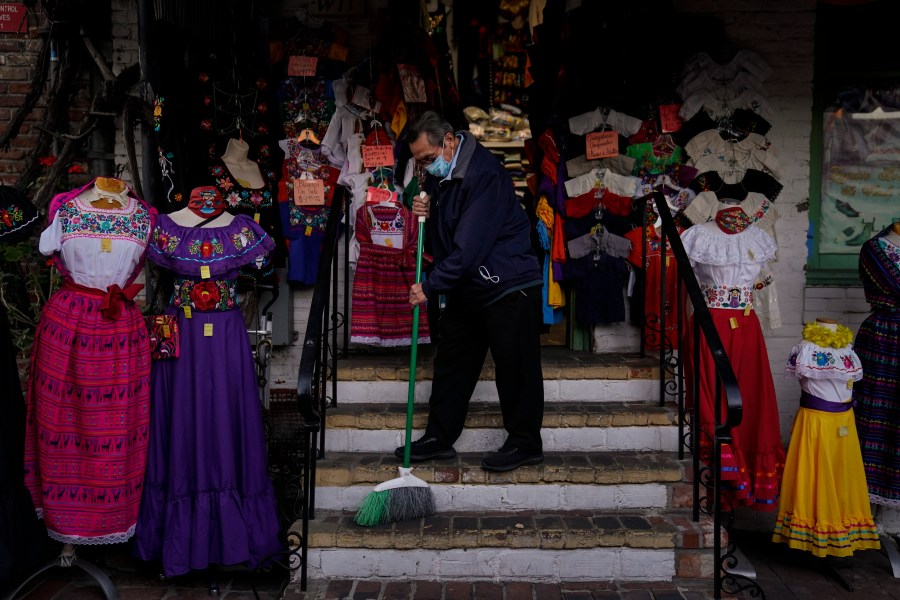 Victor Flores, 66, a third-generation owner of a gift shop, sweeps the steps of his store on Olvera Street in downtown Los Angeles on Dec. 16, 2020. (Jae C. Hong / Associated Press)