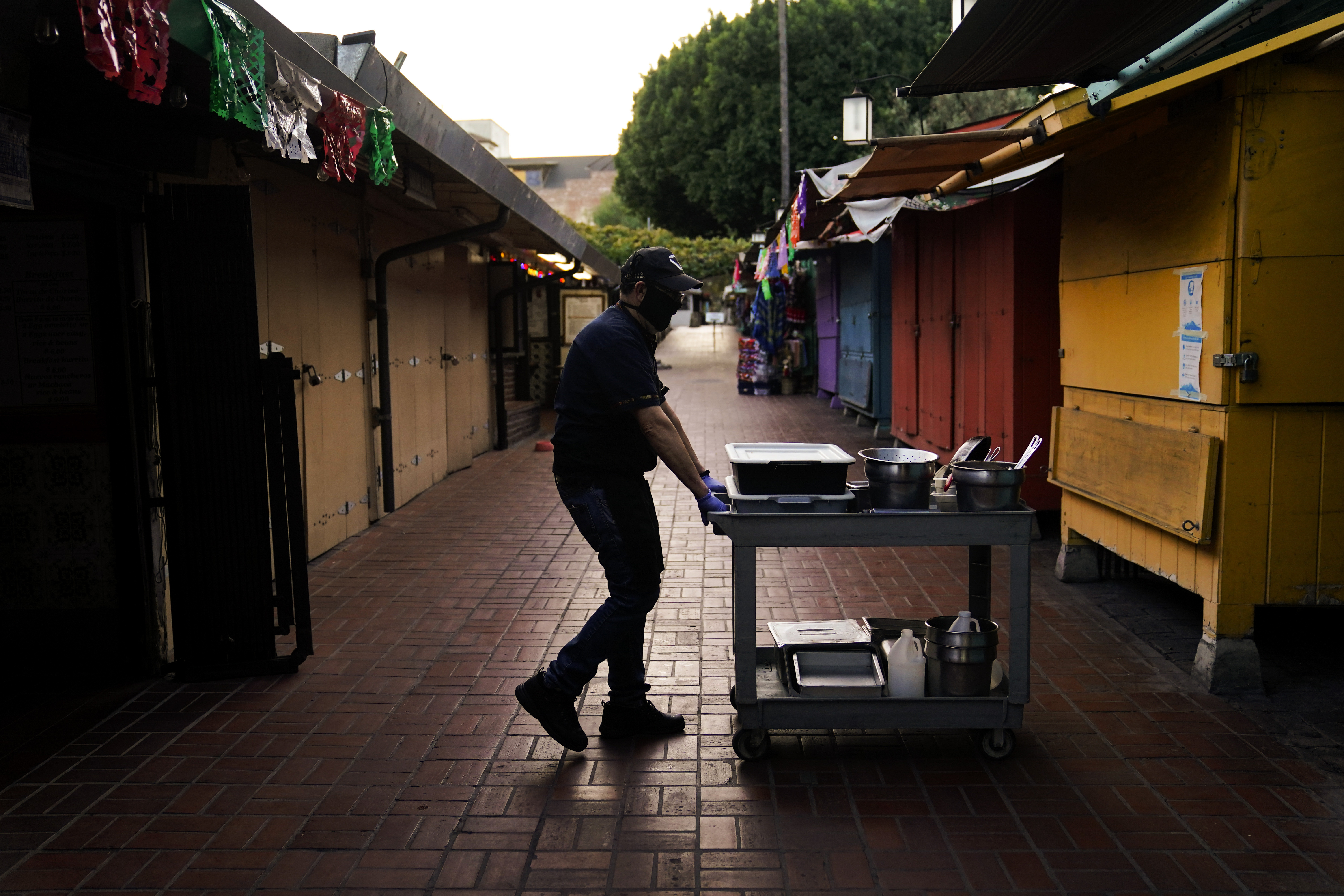 Edward Flores, 56, a fourth-generation owner of Juanita's Cafe, pushes his cart through empty Olvera Street after closing his restaurant for the day in downtown Los Angeles, Wednesday, Dec. 16, 2020. "It's pretty grim right now," said Flores. "I know of six (businesses) that have gone belly up. These are my neighbors and my friends. To see them fail through no fault of their own is heartbreaking." (AP Photo/Jae C. Hong)