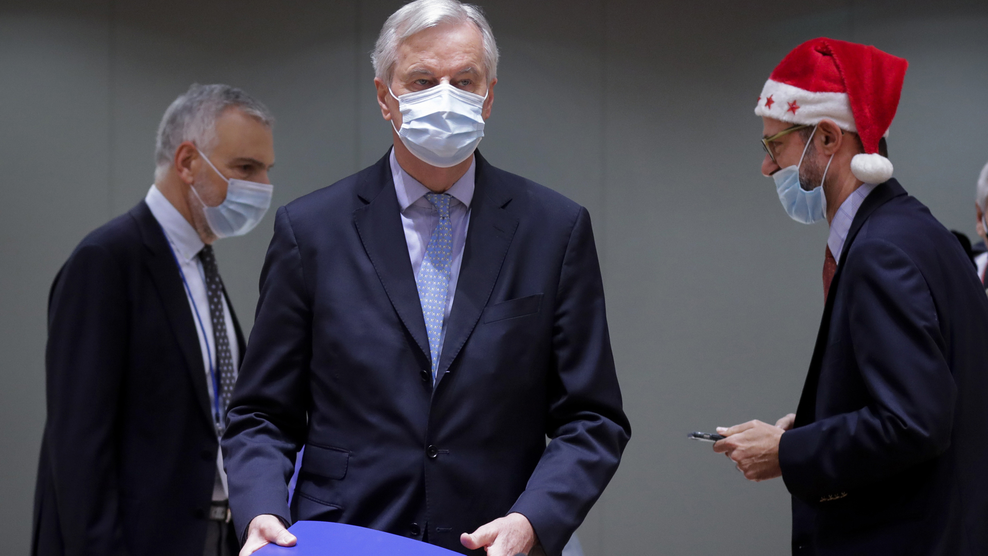 A colleague wears a Christmas hat as European Union chief negotiator Michel Barnier, center, carries a binder of the Brexit trade deal during a special meeting of Coreper, at the European Council building in Brussels on Dec. 25, 2020. (Olivier Hoslet, Pool via AP)