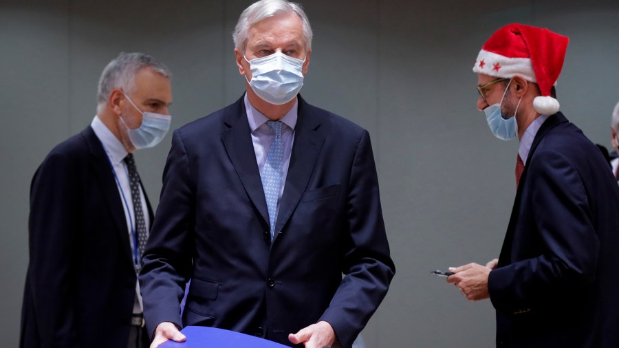 A colleague wears a Christmas hat as European Union chief negotiator Michel Barnier, center, carries a binder of the Brexit trade deal during a special meeting of Coreper, at the European Council building in Brussels on Dec. 25, 2020. (Olivier Hoslet, Pool via AP)