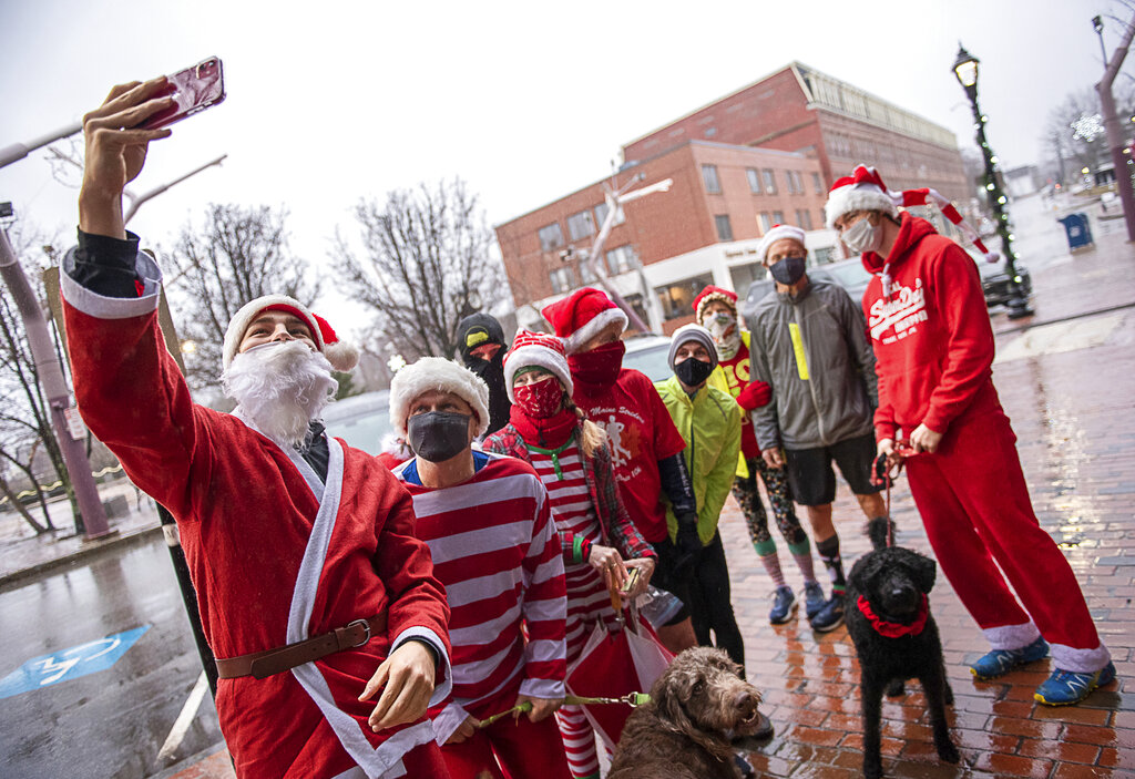 Maxi Kolb, an exchange student from Germany, takes a photo of a group of Santas and elves getting ready for their annual Christmas morning run on Main Street in Auburn, Maine on Dec. 25, 2020. (Andree Kehn/Sun Journal via AP)