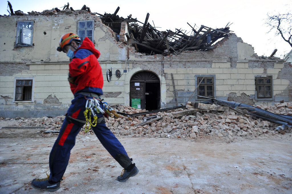 A rescuer walks past a building damaged in an earthquake in Petrinja, Croatia, Tuesday, Dec. 29, 2020. (AP Photo)