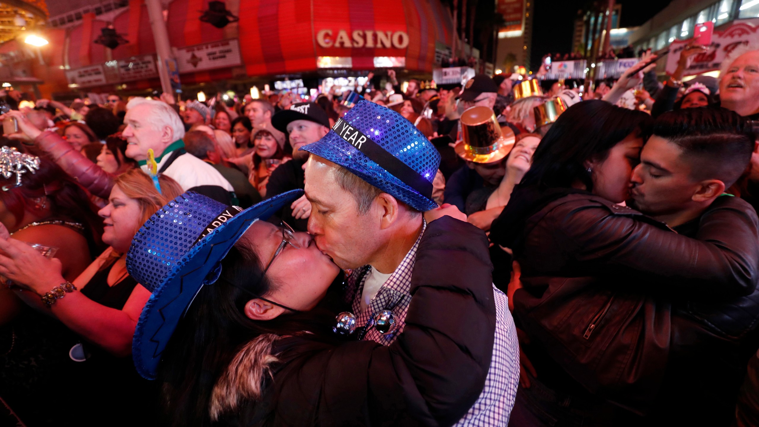 In this Jan. 1, 2018, file photo, newlyweds Alison and Kenny Finchum, lower left, of Tulsa, Okla., kiss just after midnight during a New Year's party at the Fremont Street Experience in downtown Las Vegas. (Steve Marcus/Las Vegas Sun via AP)