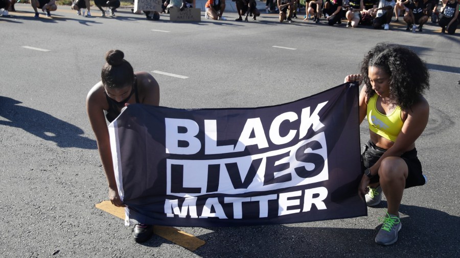 In this July 11, 2020 file photo, Alycia Pascual-Pena, left, and Marley Ralph kneel while holding a Black Lives Matter banner during a protest in memory of Breonna Taylor, in Los Angeles. Taylor was killed in her apartment by members of the Louisville, Ky., Metro Police Department on March 13. (AP Photo/Marcio Jose Sanchez, File)