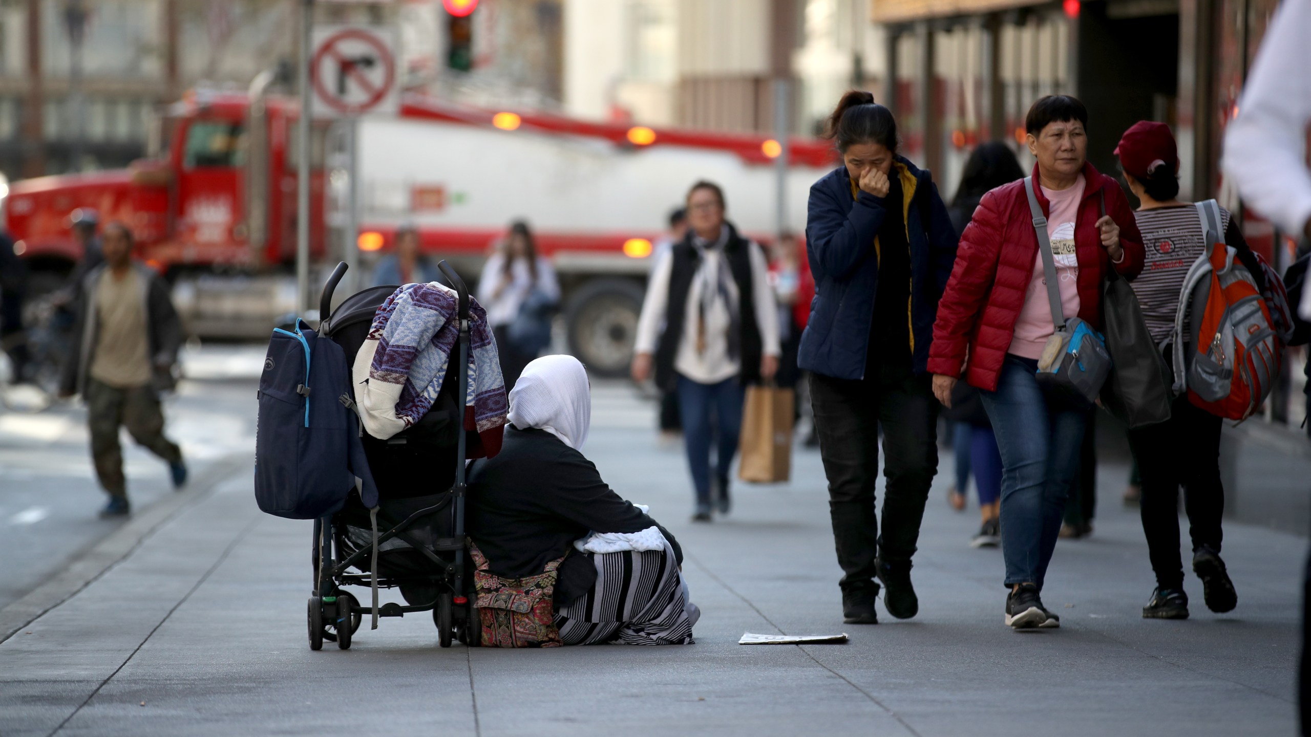 A homeless woman begs for change as pedestrians walk by on November 25, 2019 in San Francisco, California. (Justin Sullivan/Getty Images)