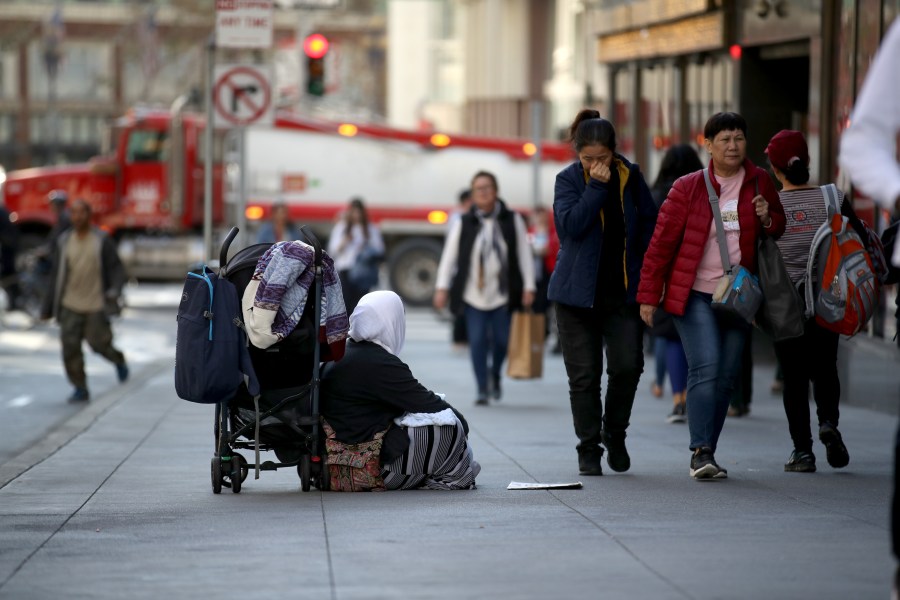 A homeless woman begs for change as pedestrians walk by on November 25, 2019 in San Francisco, California. (Justin Sullivan/Getty Images)