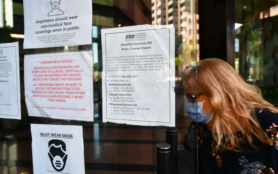 A woman wearing a facemask enters a building where the Employment Development Department has its offices in Los Angeles, California on May 4, 2020, past a posted sign mentioning the closure of the offices's public access counters due to the coronavirus pandemic. (Frederic J. Brown/AFP via Getty Images)