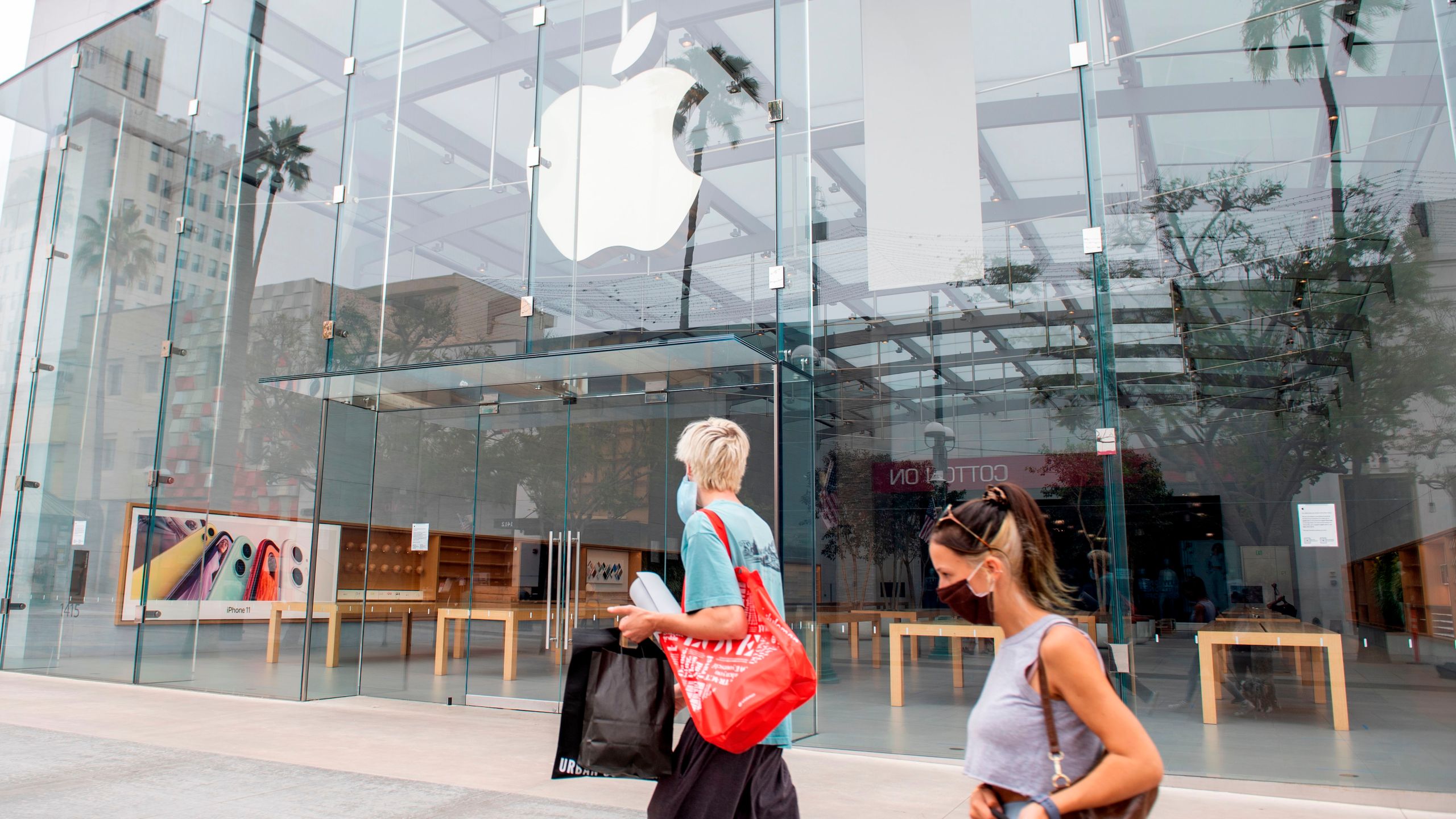 People wearing a mask walk by a closed Apple Store in Santa Monica, California, on July 28, 2020. (VALERIE MACON/AFP via Getty Images)