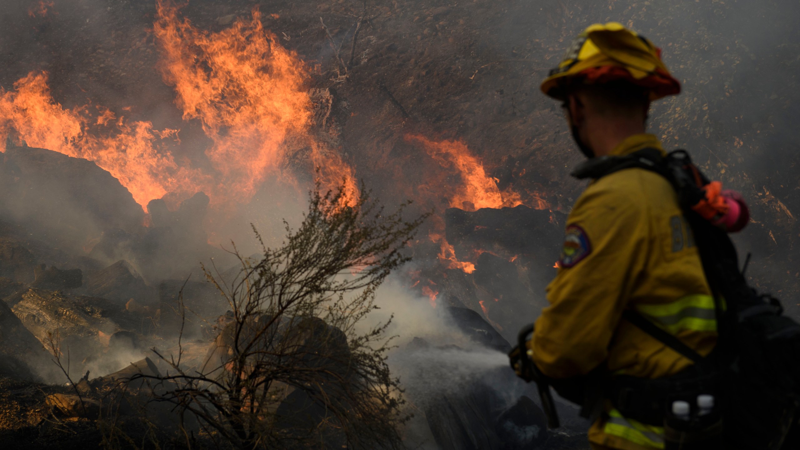 A Brea firefighter sprays water to contain the Bond Fire as it burns debris behind a structure near Lake Forest, California, on Dec. 3, 2020. (Patrick T. Fallon /AFP via Getty Images)