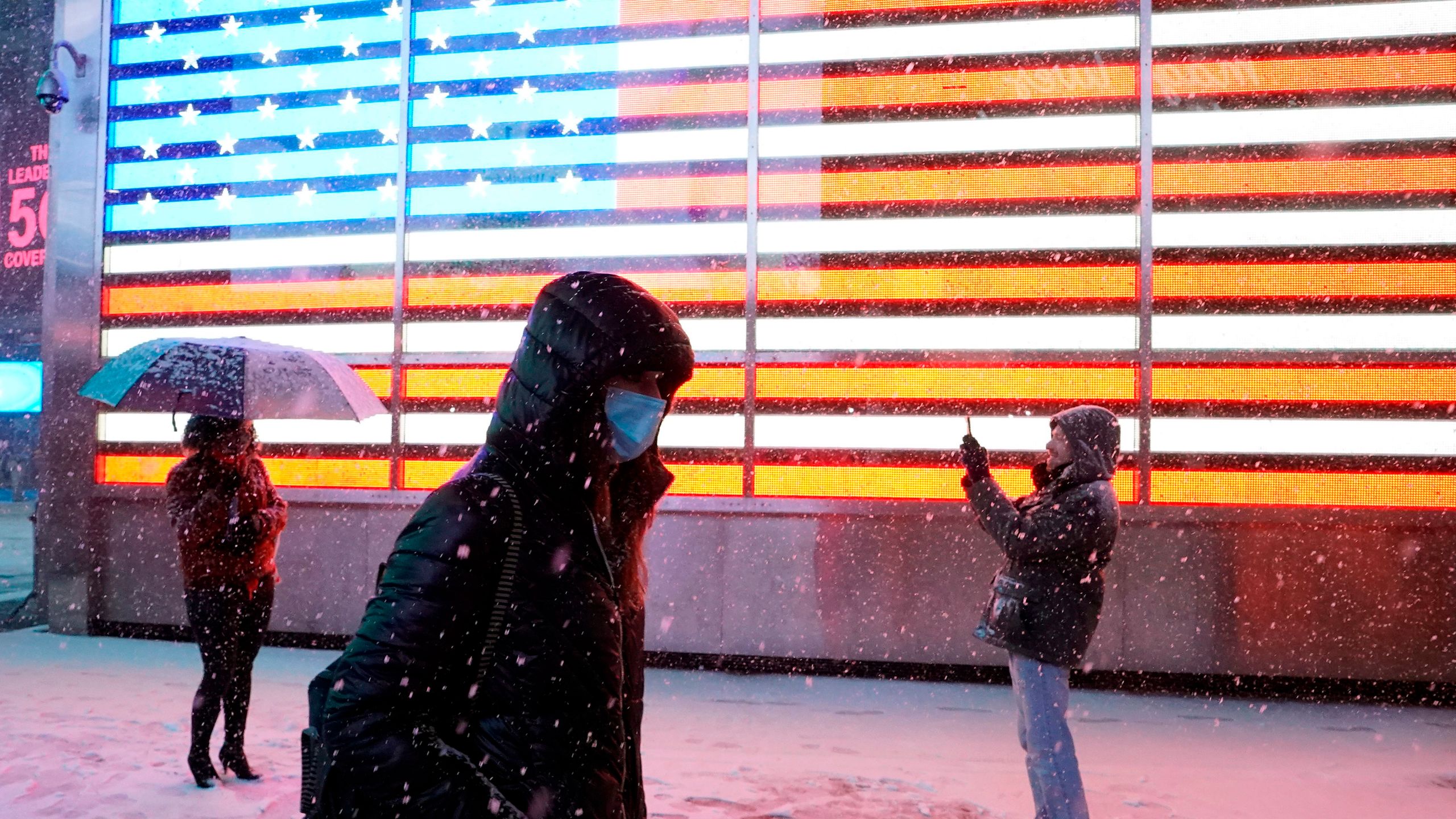 A person poses under the snow in front of a screen showing a U.S. flag in Times Square in New York City on Dec. 16, 2020 as Storm Gail hits the East coast. (TIMOTHY A. CLARY/AFP via Getty Images)