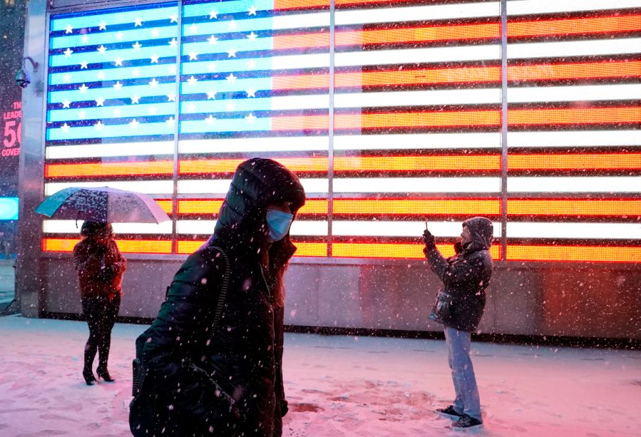 A person poses under the snow in front of a screen showing a U.S. flag in Times Square in New York City on Dec. 16, 2020 as Storm Gail hits the East coast. (TIMOTHY A. CLARY/AFP via Getty Images)