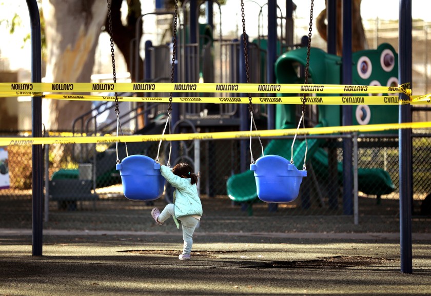 Maala Sampath, 2, tries to climb into a swing before her nanny reminds her that the playground is closed at Glen Anderson Park in Redondo Beach on Dec. 1, 2020. (Christina House / Los Angeles Times)