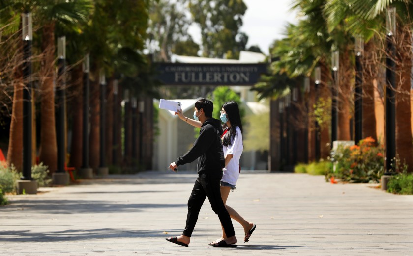 Two students wearing masks walk on the Cal State Fullerton campus in 2020. (Christina House / Los Angeles Times)