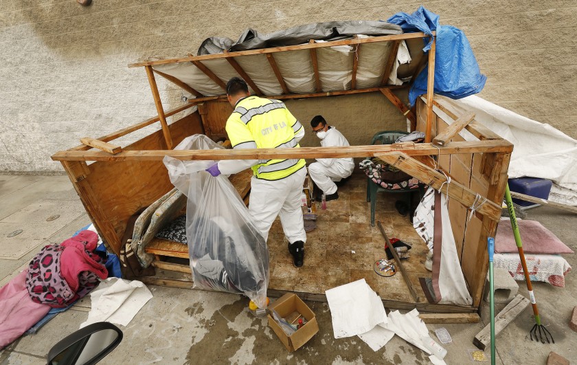 Sanitation workers Jesus Sanchez, left, and Javier Villareal check a homeless encampment for hazardous materials in 2019. (Al Seib / Los Angeles Times)