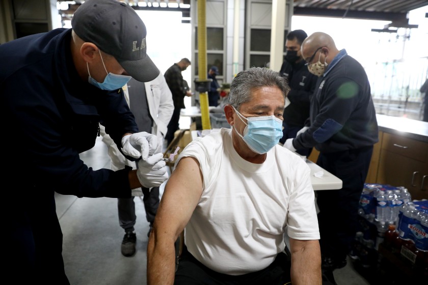 Firefighter paramedic Matthew Kovar, left, administers a COVID-19 vaccination to fire inspector Gabriel Orona at the Los Angeles Fire Department Station 4 on Dec. 28, 2020. (Gary Coronado / Los Angeles Times)