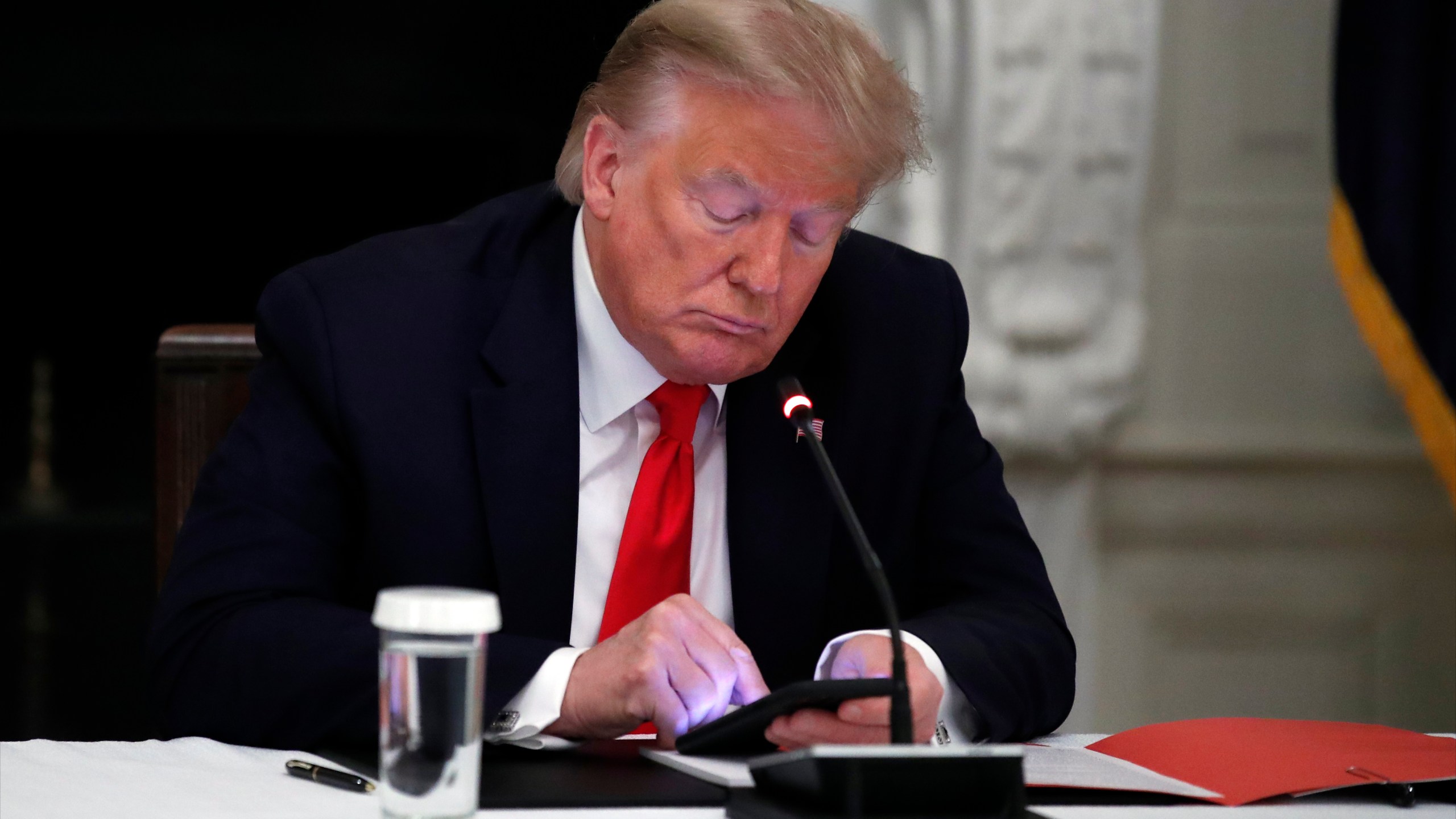 In this Thursday, June 18, 2020 file photo, President Donald Trump looks at his phone during a roundtable with governors on the reopening of America's small businesses, in the State Dining Room of the White House in Washington. (AP Photo/Alex Brandon, File)