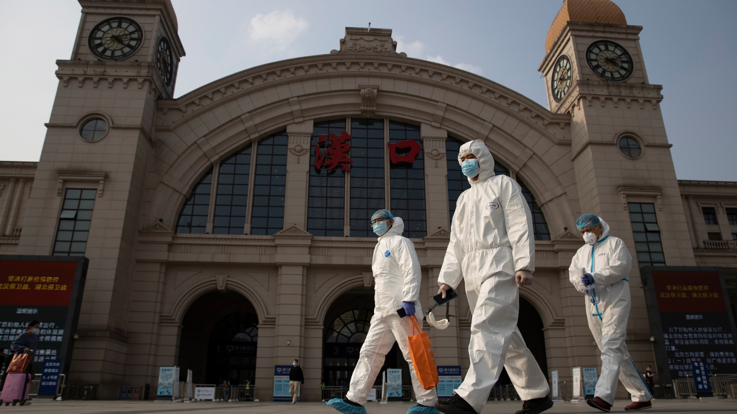 In this April 7, 2020, file photo, workers in protective suits walk past the Hankou railway station on the eve of its resuming outbound traffic in Wuhan in central China's Hubei province. (AP Photo/Ng Han Guan)