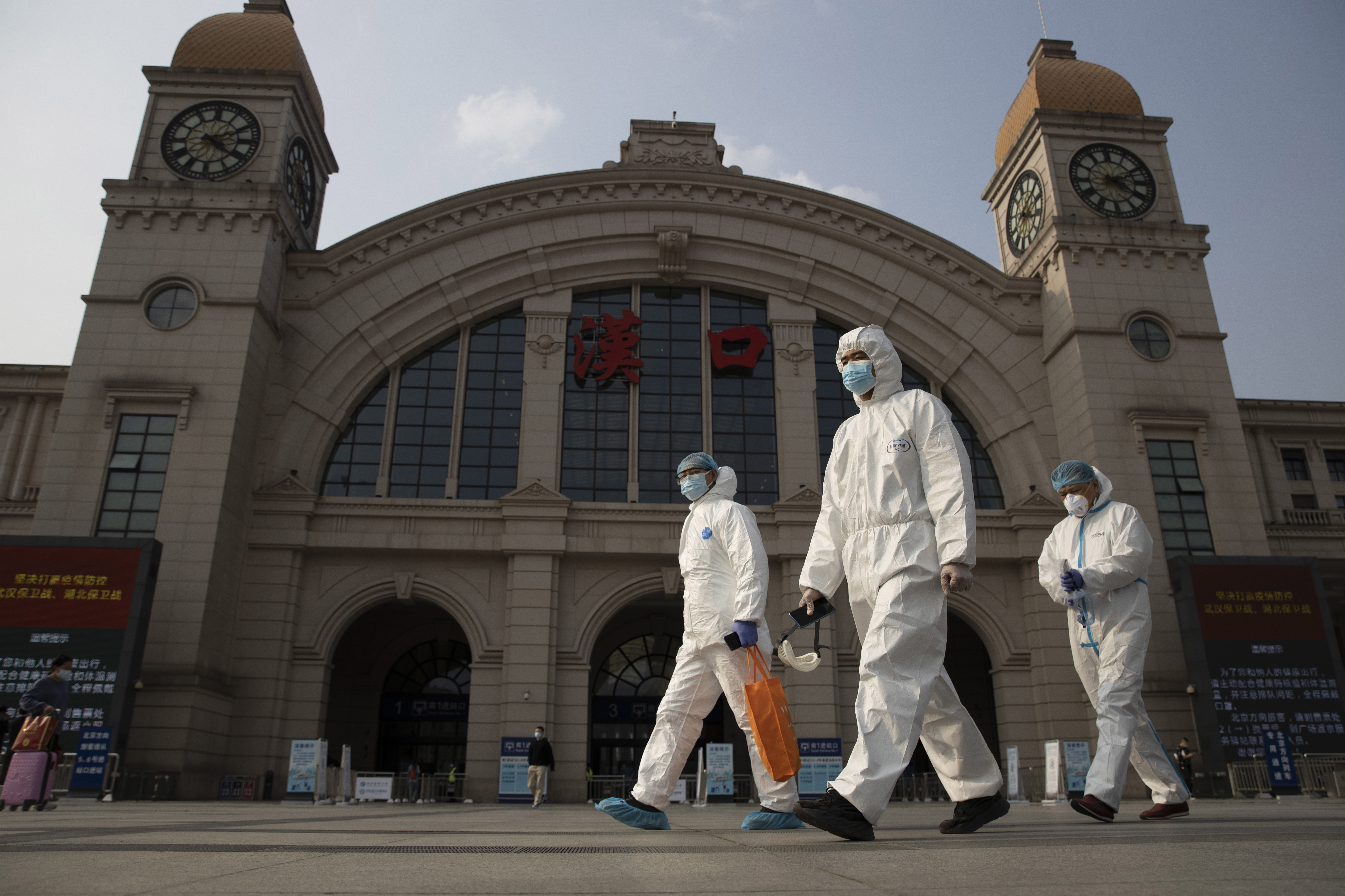 In this April 7, 2020, file photo, workers in protective suits walk past the Hankou railway station on the eve of its resuming outbound traffic in Wuhan in central China's Hubei province. (AP Photo/Ng Han Guan)