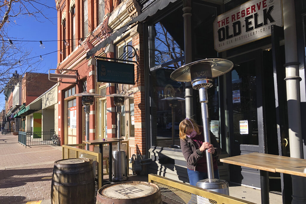 Whiskey tasting room manager Melinda Maddox moves a propane-fueled outdoor space heater in downtown Fort Collins, Colo., in preparation for opening on Jan. 6, 2021. (AP Photo/Mead Gruver)