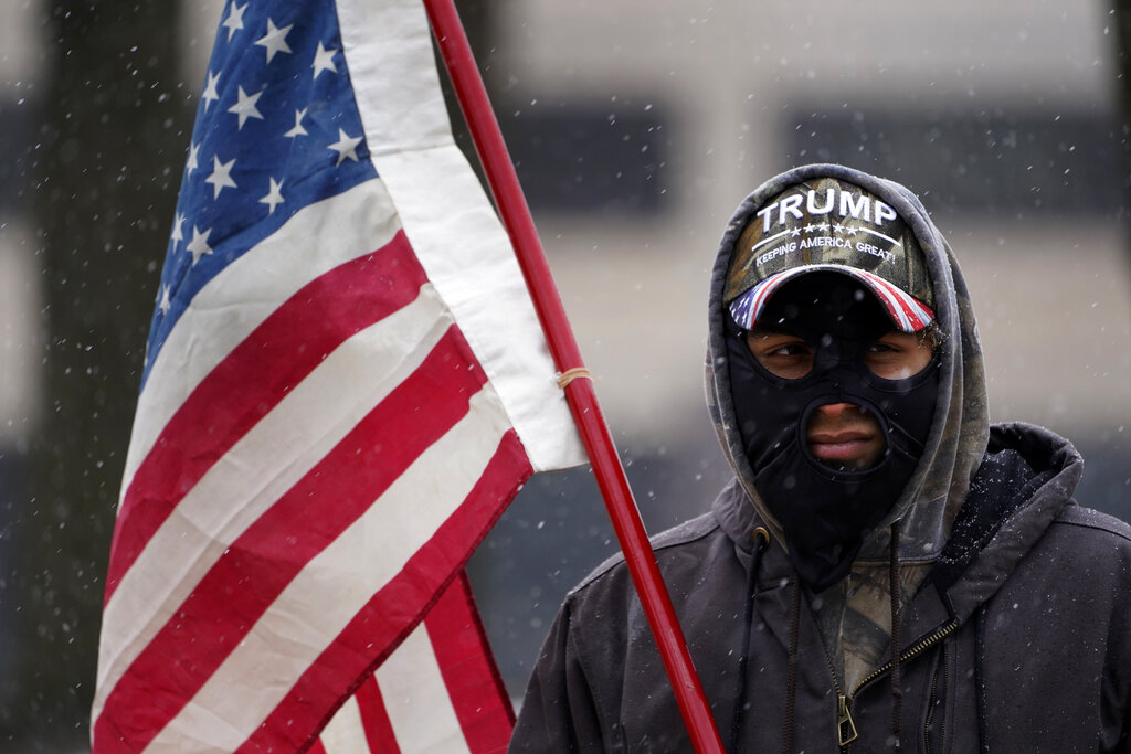 A man stands outside the state capitol wearing a Trump hat with an American flag in Lansing, Mich., Sunday, Jan. 17, 2021. (AP Photo/Paul Sancya)