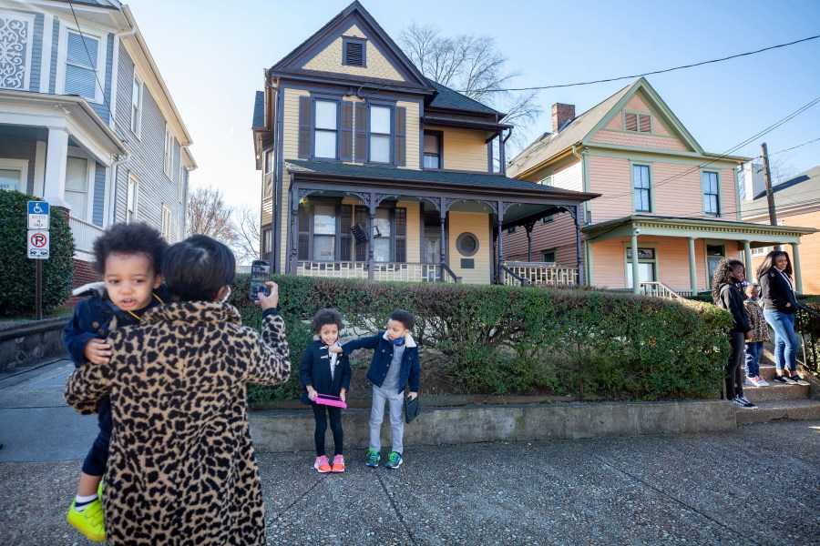 Alexis Upshaw, left, holding 2-year-old Ari Upshaw, takes a photo as Ty Upshaw, 7, right, adjusts the mask of his sister, Mila Upshaw, 5, in front of the birthplace of Dr. Martin Luther King, Jr. on Monday, Jan. 18, 2021, the Martin Luther King Jr. holiday, in Atlanta. (AP Photo/Branden Camp)