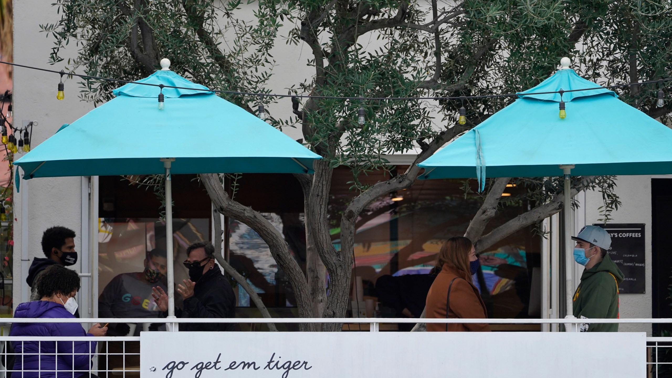 People wear masks as they wait outdoors for takeaway coffee and eats at the "go get em tiger" coffee bar on Hollywood Blvd., in Los Angeles Monday, Jan. 25, 2021. California has lifted regional stay-at-home orders statewide in response to improving coronavirus conditions. Public health officials said Monday that the state will return to a system of county-by-county restrictions intended to stem the spread of the virus. (AP Photo/Damian Dovarganes)