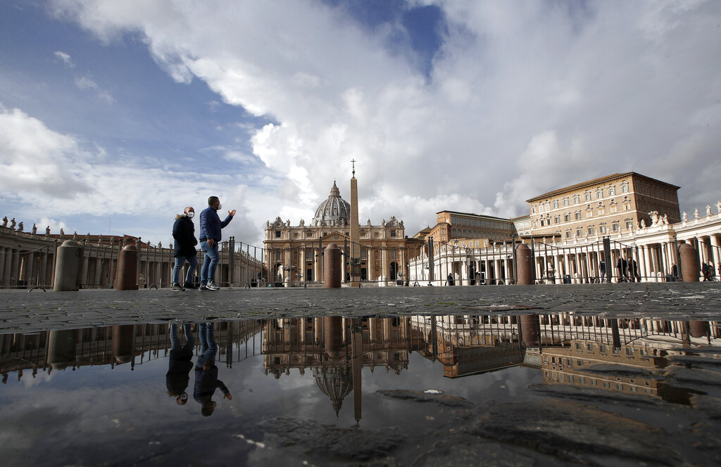 People are reflected on a puddle as they walk in an empty St.Peter's Square, as Pope Francis is reciting the Angelus noon prayer in his studio in the Apostolic palace, seen on the right, at the Vatican, Sunday, Jan. 31, 2021. (AP Photo/Alessandra Tarantino)