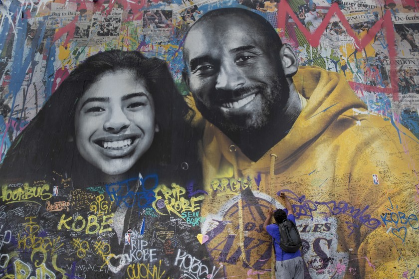 A man writes a message on a mural honoring Kobe Bryant and his daughter Gianna in Los Angeles in February 2020. (Mel Melcon / Los Angeles Times)