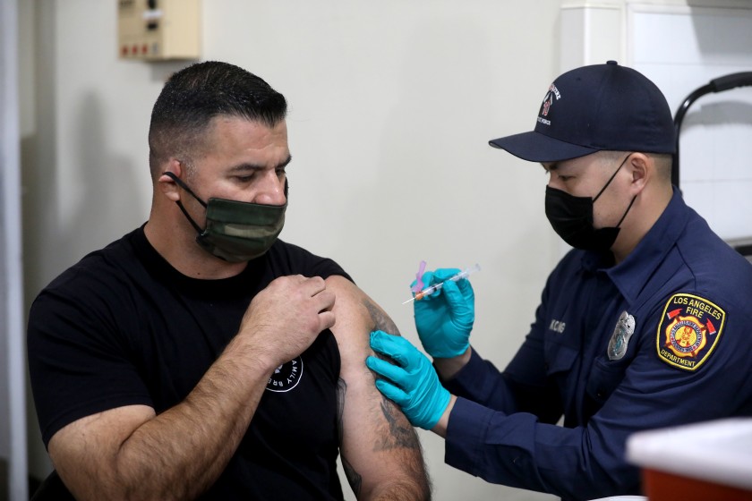 L.A. Fire Department Capt. Elliot Ibanez, left, is given a Moderna COVID-19 vaccination from LAFD paramedic Anthony Kong on Monday at Station 4 in Los Angeles. (Los Angeles Times)