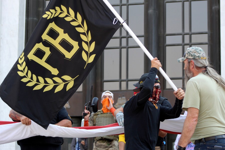 In this Sept. 7, 2020, file photo, a protester carries a Proud Boys banner, a right-wing group, while other members start to unfurl a large U.S. flag in front of the Oregon State Capitol in Salem. (Andrew Selsky/Associated Press)