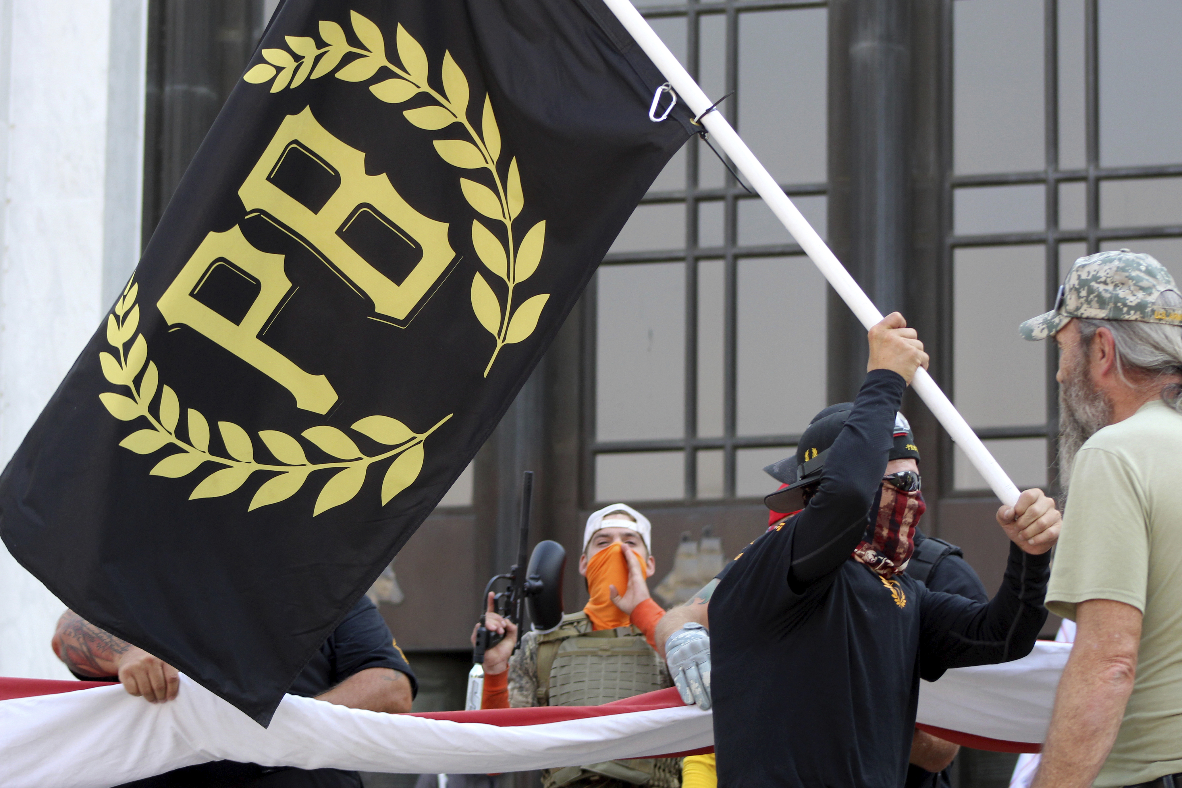 In this Sept. 7, 2020, file photo, a protester carries a Proud Boys banner, a right-wing group, while other members start to unfurl a large U.S. flag in front of the Oregon State Capitol in Salem, Ore. The Canadian government designated the Proud Boys group as a terrorist entity on Wednesday, Feb. 3, 2021, noting they played a pivotal role in the insurrection at the U.S. Capitol on Jan. 6. (AP Photo/Andrew Selsky, File)