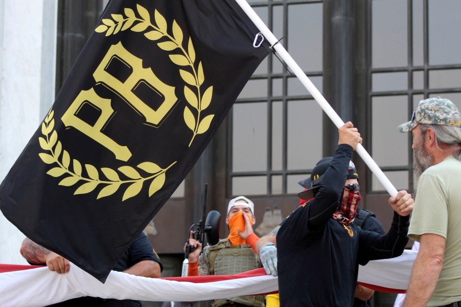 In this Sept. 7, 2020, file photo, a protester carries a Proud Boys banner, a right-wing group, while other members start to unfurl a large U.S. flag in front of the Oregon State Capitol in Salem, Ore. The Canadian government designated the Proud Boys group as a terrorist entity on Wednesday, Feb. 3, 2021, noting they played a pivotal role in the insurrection at the U.S. Capitol on Jan. 6. (AP Photo/Andrew Selsky, File)