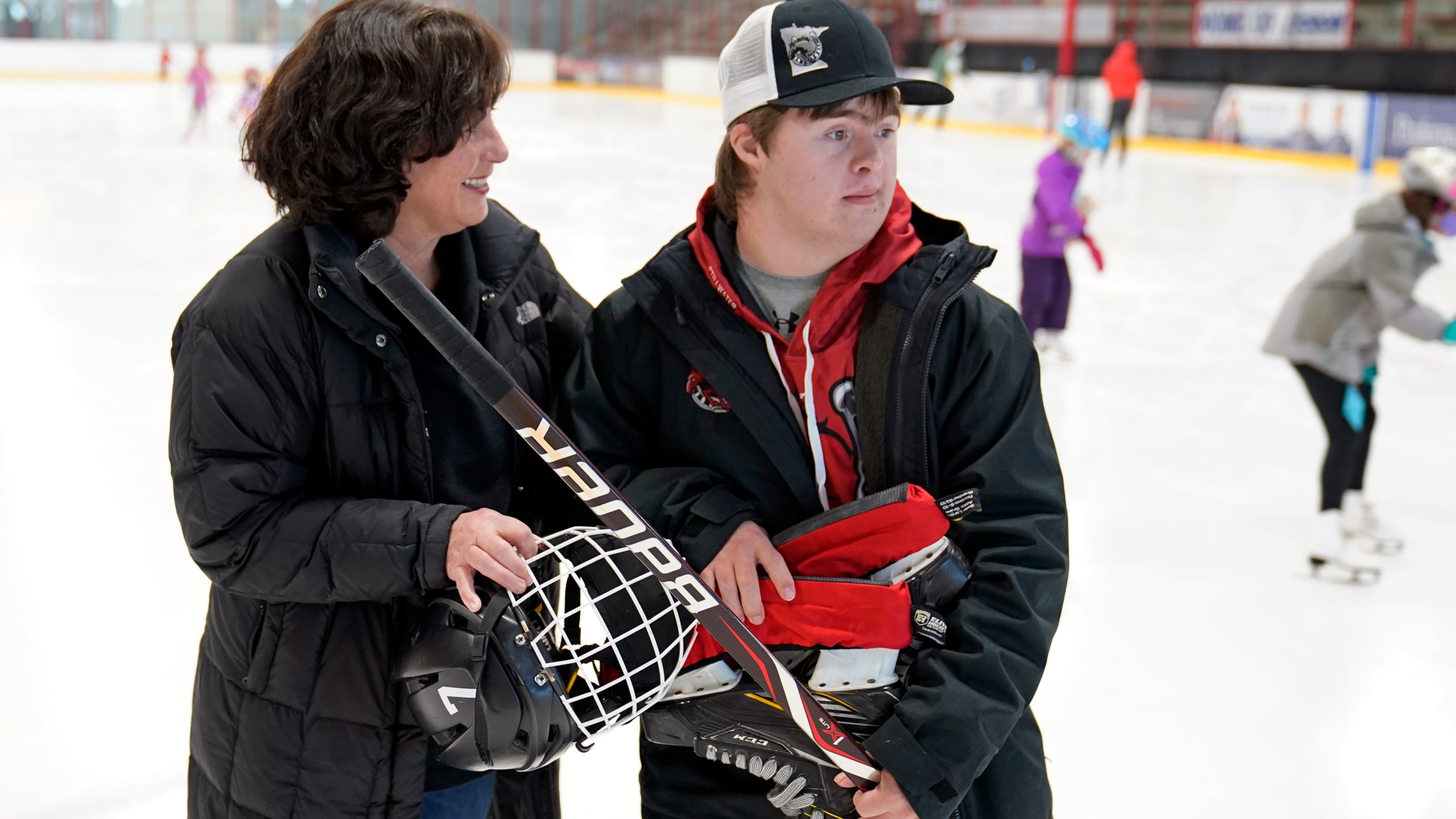 Suzy Lindeberg poses with her 20-year-old son John on a hockey rink, Tuesday, Feb. 9, 2021, in Stillwater, Minn. John, who has Down Syndrome, can't spend as much time at the rink as he used to since he is at higher risk for hospitalization or death if he caught COVID-19, but his mother and other advocates worry that the state of Minnesota has placed people with disabilities too far down the priority list. (AP Photo/Jim Mone)