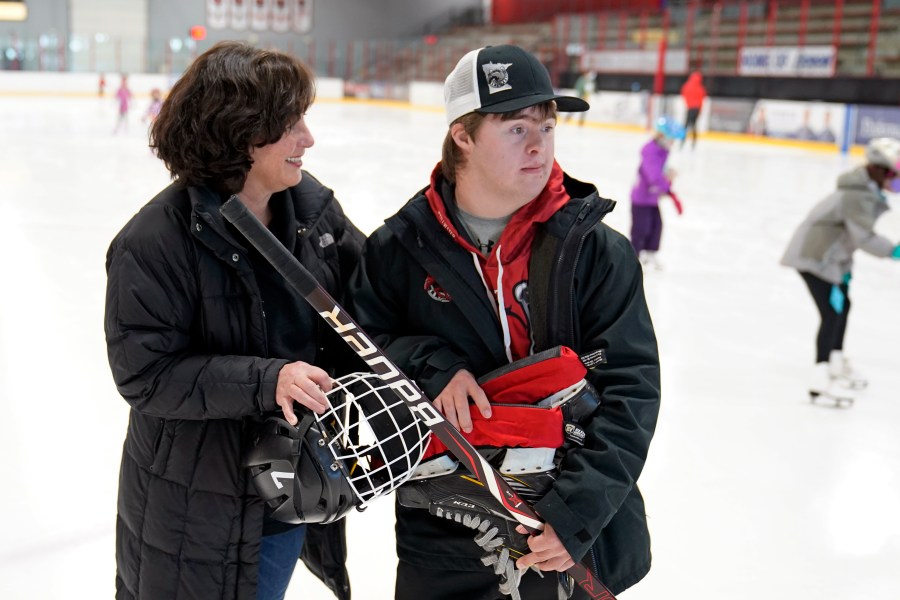 Suzy Lindeberg poses with her 20-year-old son John on a hockey rink, Tuesday, Feb. 9, 2021, in Stillwater, Minn. John, who has Down Syndrome, can't spend as much time at the rink as he used to since he is at higher risk for hospitalization or death if he caught COVID-19, but his mother and other advocates worry that the state of Minnesota has placed people with disabilities too far down the priority list. (AP Photo/Jim Mone)