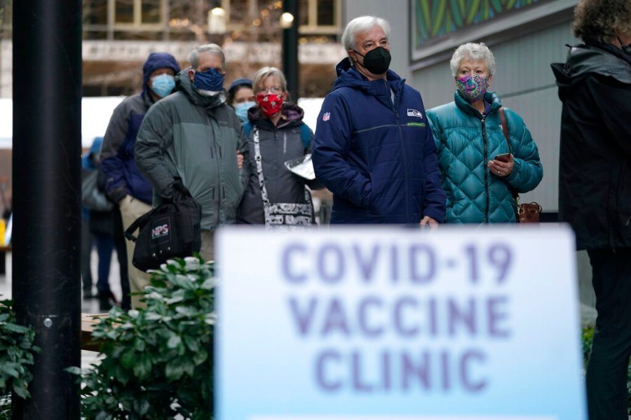 In this Jan. 24, 2021, file photo, people stand near a sign as they wait in line to receive the first of two doses of the Pfizer vaccine for COVID-19 at a one-day vaccination clinic set up in an Amazon.com facility in Seattle. (AP Photo/Ted S. Warren, File)