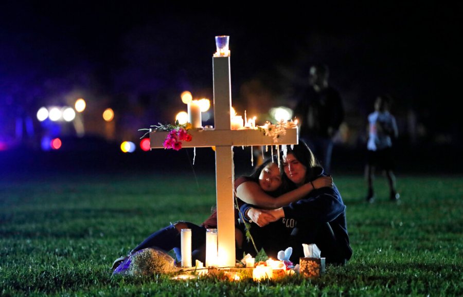 In this Feb. 15, 2018 file photo, people comfort each other as they sit and mourn at one of seventeen crosses, after a candlelight vigil for the victims of the shooting at Marjory Stoneman Douglas High School, in Parkland, Fla. (AP Photo/Gerald Herbert, File)