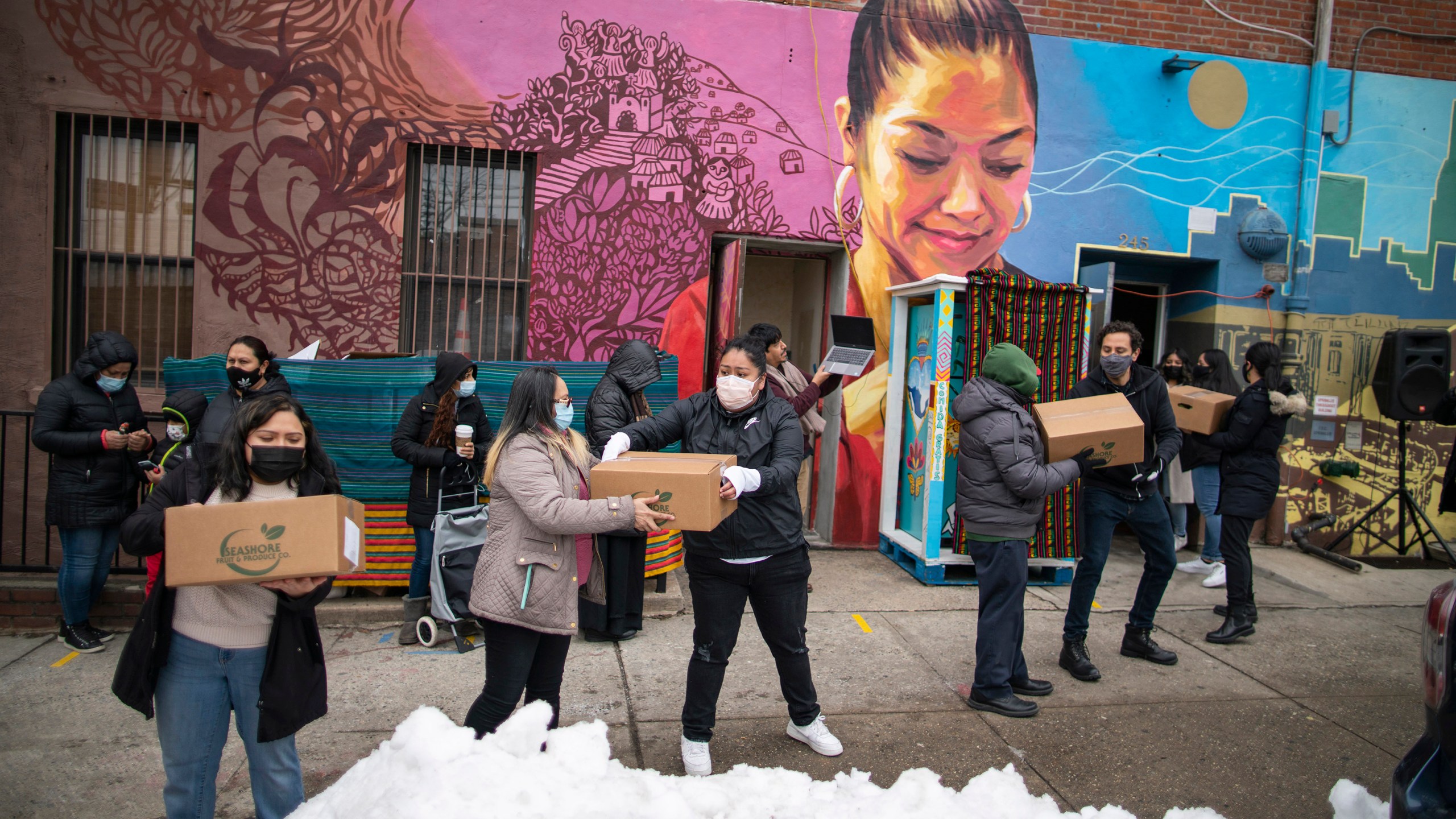 Volunteers carry food for donations as people receive COVID-19 information for vaccines at the community center Mixteca during the coronavirus pandemic, Saturday, Feb. 13, 2021, in the Brooklyn borough of New York. (AP Photo/Eduardo Munoz Alvarez)