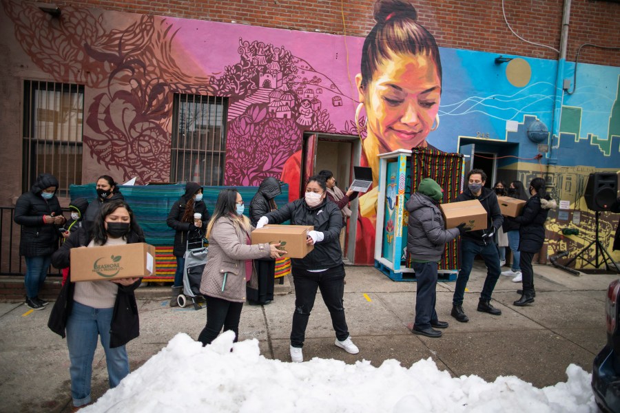 Volunteers carry food for donations as people receive COVID-19 information for vaccines at the community center Mixteca during the coronavirus pandemic, Saturday, Feb. 13, 2021, in the Brooklyn borough of New York. (AP Photo/Eduardo Munoz Alvarez)