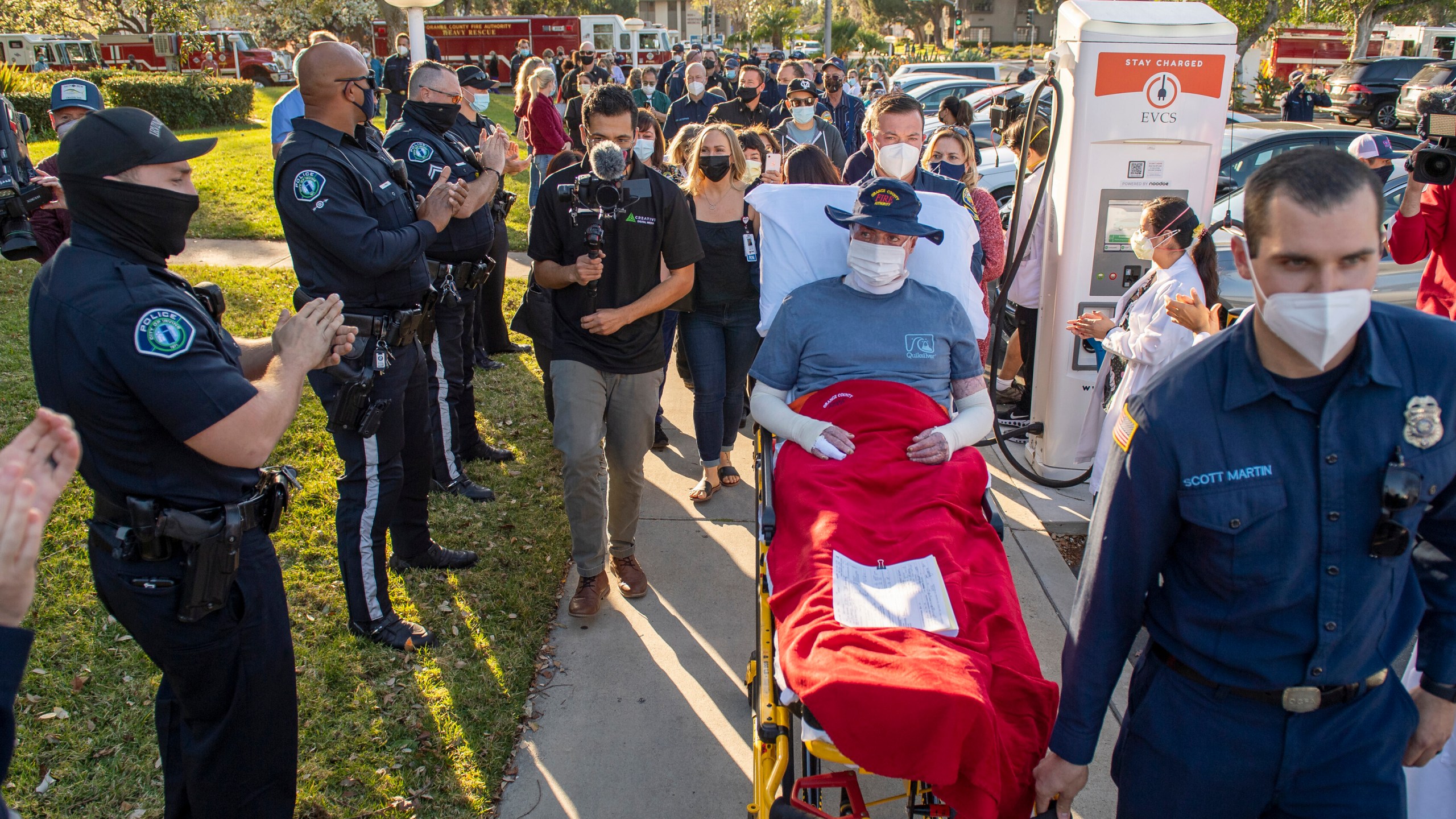 Dylan Van Iwaarden, an Orange County Fire Authority hand crew firefighter, is wheeled on a gurney as he leaves the Orange County Global Medical Center as scores of firefighters, police and medical personal line the sidewalk to cheer him on in Santa Ana on Feb. 17, 2021. (Leonard Ortiz / The Orange County Register via Associated Press)