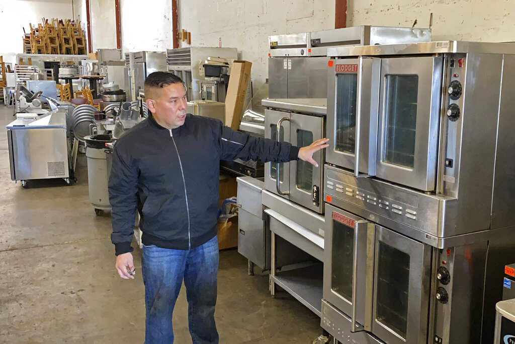 Jose Bonilla Jr. shows a used industrial oven for sale in the warehouse of his family's business, American Restaurant Supply in San Leandro, Calif., on Jan. 14, 2021. The pandemic has forced thousands of restaurants to permanently shut their doors as dining restrictions keep customers away. But the unprecedented closures have created a business boom for commercial auctioneers that buy and sell used restaurant equipment. (AP Photo/Terry Chea)