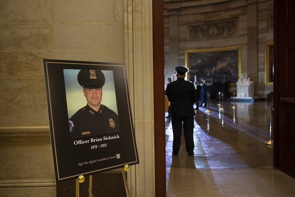 In this Feb. 2, 2021, file photo a placard is displayed with an image of the late U.S. Capitol Police officer Brian Sicknick on it as people wait for an urn with his cremated remains to be carried into the U.S. Capitol to lie in honor in the Capitol Rotunda in Washington. (Brendan Smialowski/Pool via AP, File)