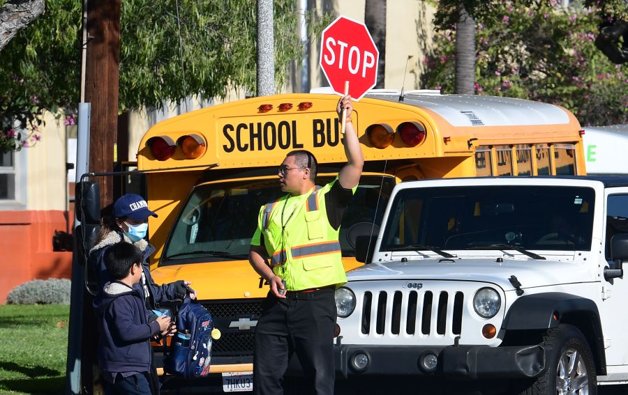 A woman wears a facemask picking up a child as an Alhambra Unified School District crossing guard stops traffic outside Ramona Elementary School on February 4, 2020 in Alhambra, California. (Photo by Frederic J. BROWN / AFP)