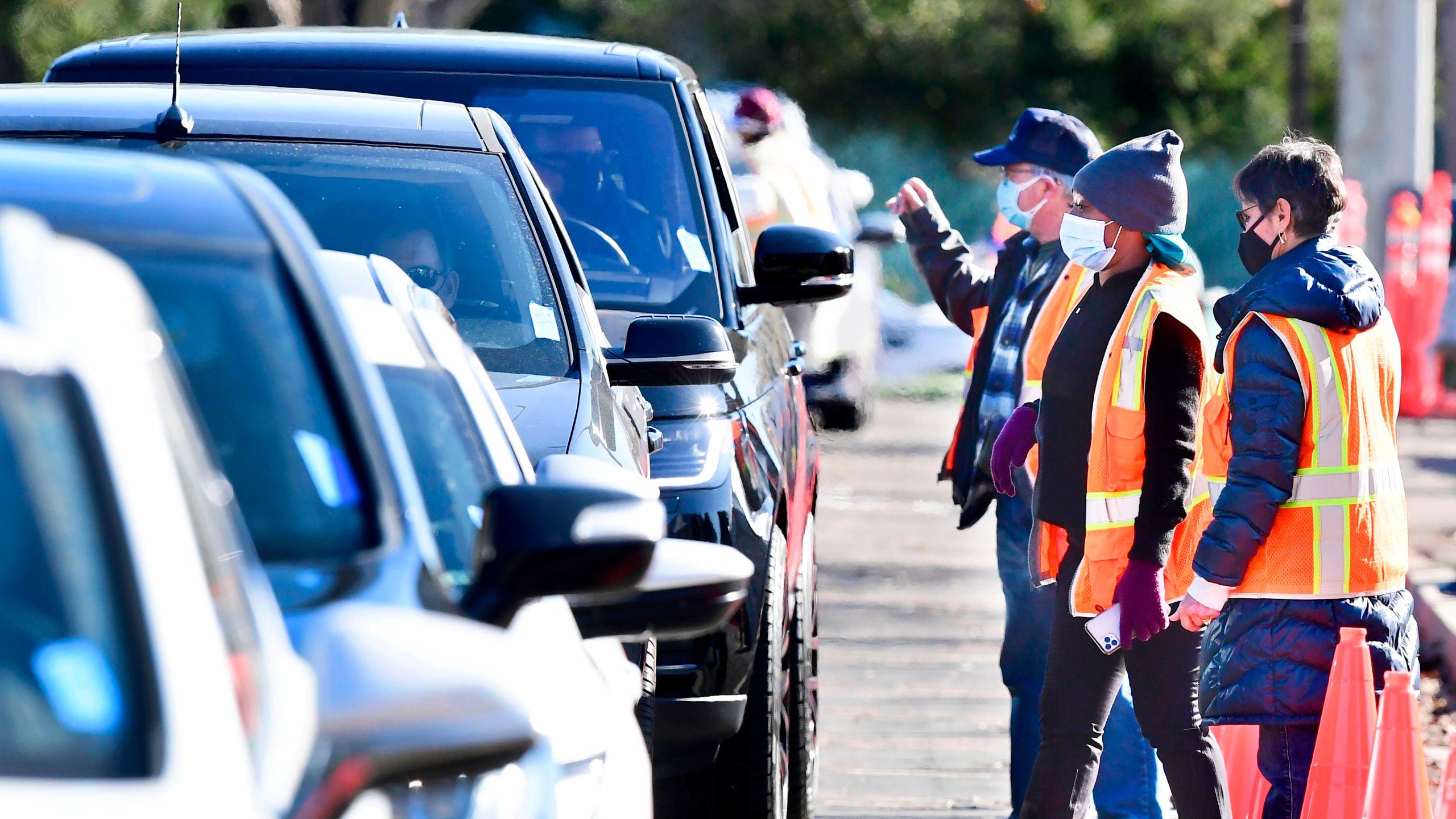 Masked volunteers assist people in their vehicles at the Cal State Northridge mass COVID-19 vaccination site in Northridge on Jan. 26, 2021. (FREDERIC J. BROWN/AFP via Getty Images)