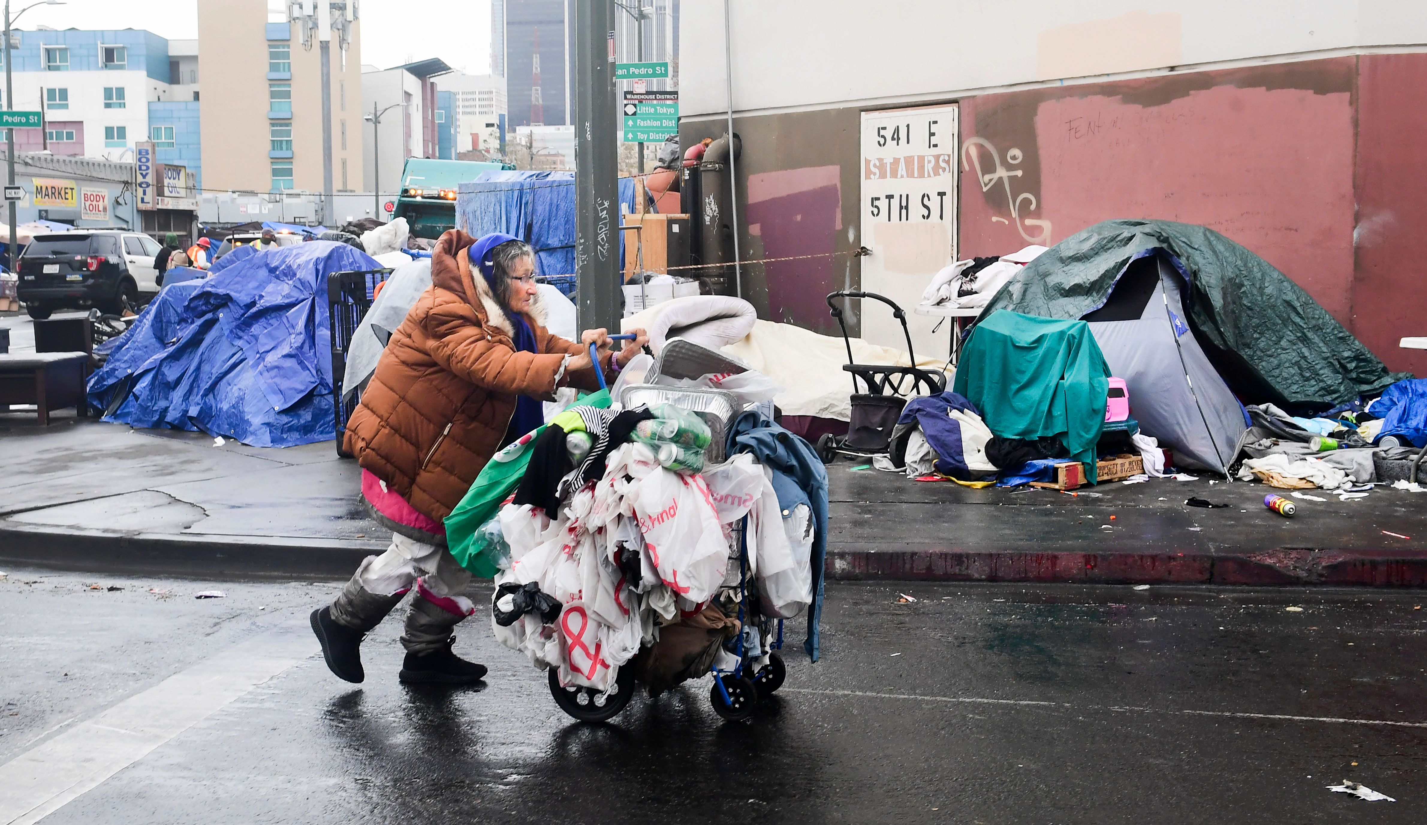 A homeless woman pushes her belongings past a row of tents on the streets of Los Angeles on Feb. 1, 2021. (Frederic J. Brown / AFP / Getty Images)