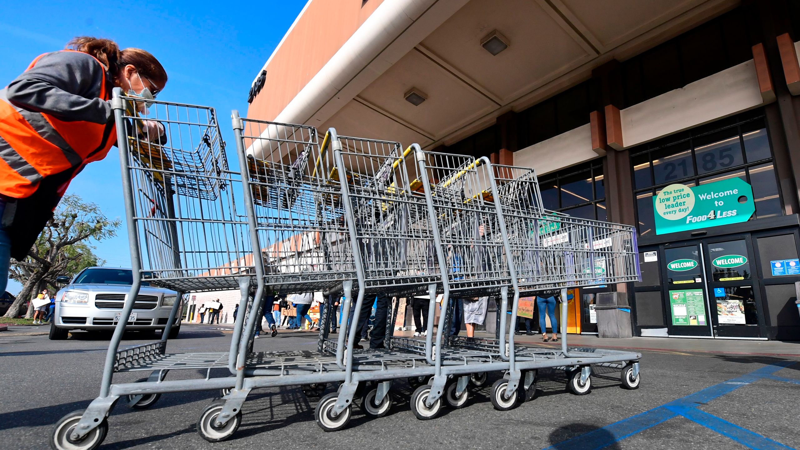 A Food 4 Less employee pushes carts past supermarket workers gathered to protest in front of the supermarket in Long Beach on Feb. 3, 2021, after a decision by owner Kroger to close two supermarkets rather than pay workers an additional $4 in "hazard pay." (Frederic J. Brown / AFP / Getty Images)