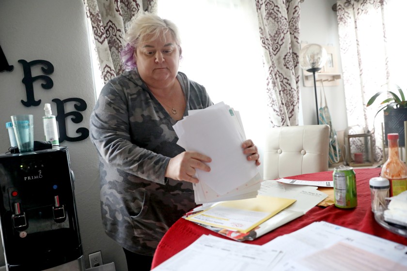 Patricia Mason, 51, displays her medical bills at her home in Vacaville, Calif. Mason works more than full time across two jobs — office administrative work, which she can do from home, and retail, which she can’t.(Gary Coronado / Los Angeles Times)