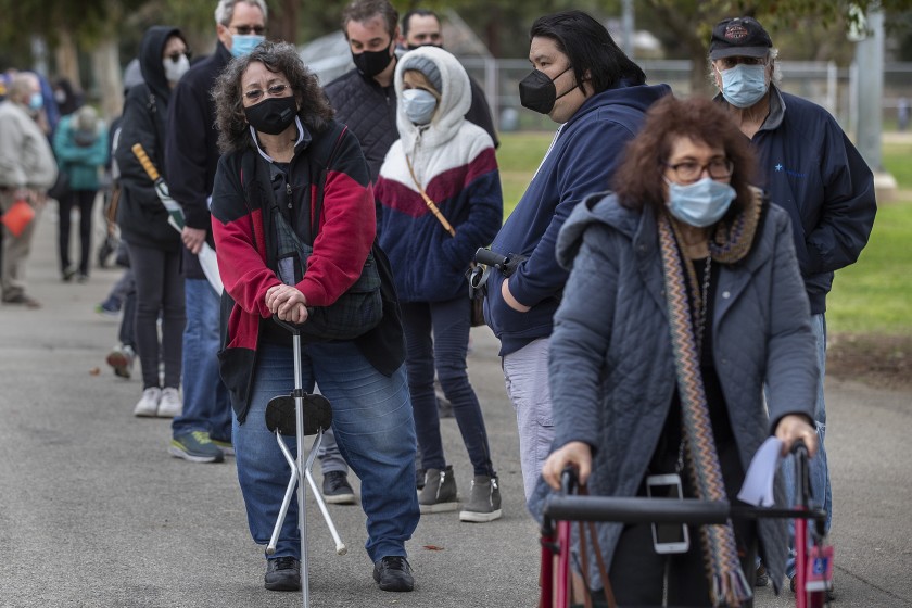 Valerie Dunlap, 67, left, of Granada Hills, and Cookie Lewis, 68, right, of Valley Village, make their way with others in the by-appointment-only line to get vaccine shots to protect against the coronavirus at the Balboa Sports Complex in Encino. (Mel Melcon/Los Angeles Times)