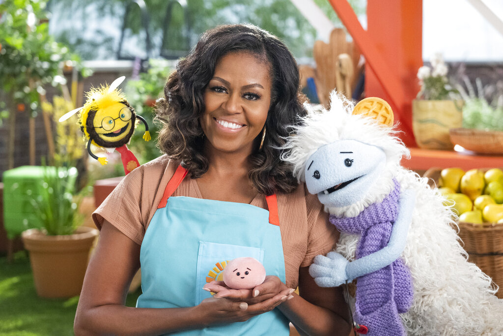 This image released by Netflix shows former first lady Michelle Obama with Busy, a bee puppet, left, Mochi, a pink round puppet, and Waffles, a furry puppet with waffle ears on the set of the children's series "Waffles + Mochi." Obama is launching the new Netflix children’s food show on March 16. (Adam Rose/Netflix via AP)