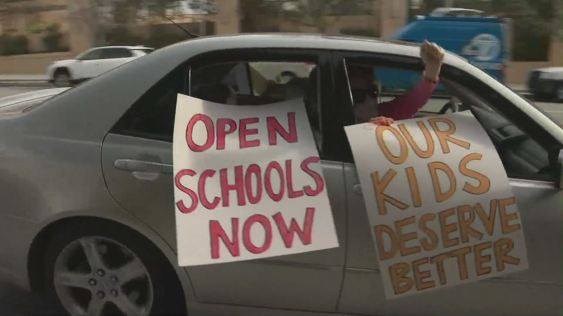 Participants of a car rally in downtown Los Angeles on Feb. 15, 2021 hold signs that read "Open schools now" and "Our kids deserve better!" (KTLA)